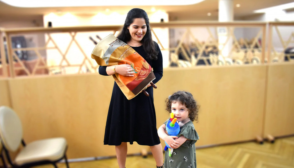 Une femme juive orthodoxe tient un rouleau de la Torah tandis que sa fille embrasse un jouet de la Torah. / RNS